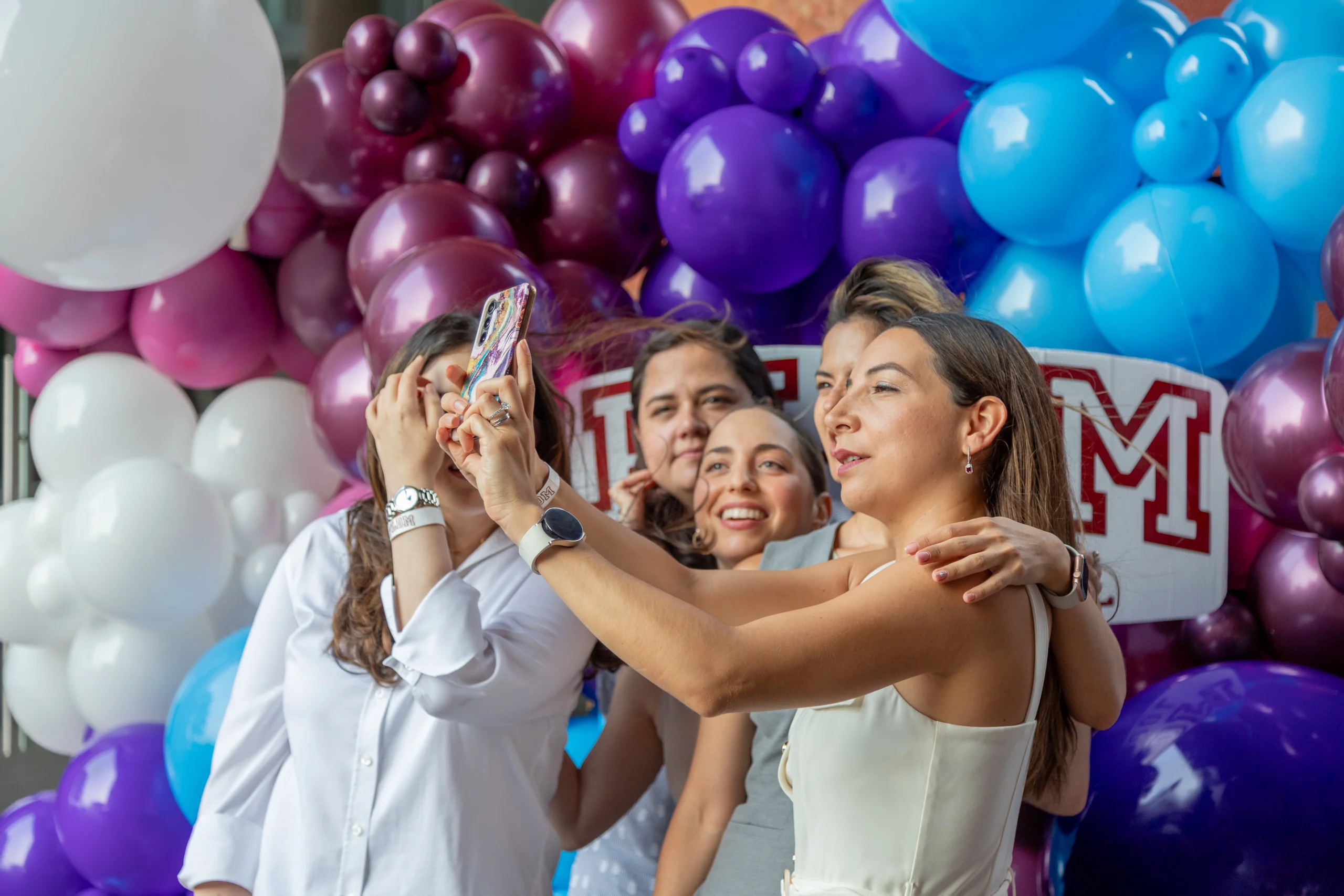 Grupo de mujeres se toma una selfie frente a un arco de globos de la FLDM durante una celebracion